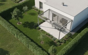 Vue aérienne d'une maison entourée d'un jardin verdoyant, mettant en avant une pergola bioclimatique en aluminium positionnée le long d'un mur, protégée par des haies brise-vent. Cette installation est conçue pour résister aux conditions de vent fort, offrant un espace extérieur agréable même en cas de tempête.